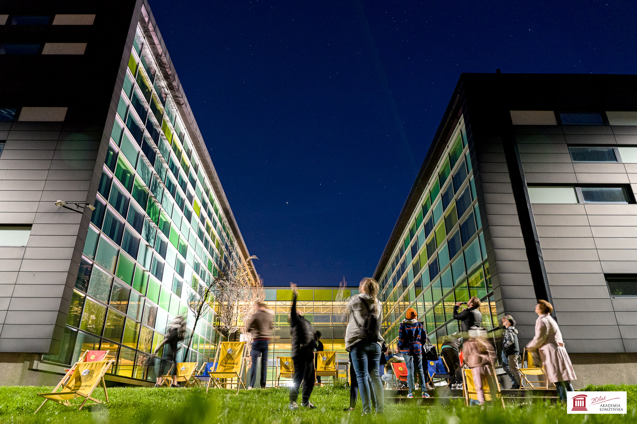Ludzie obserwóją niebo nocą przed budynkiem uczelni