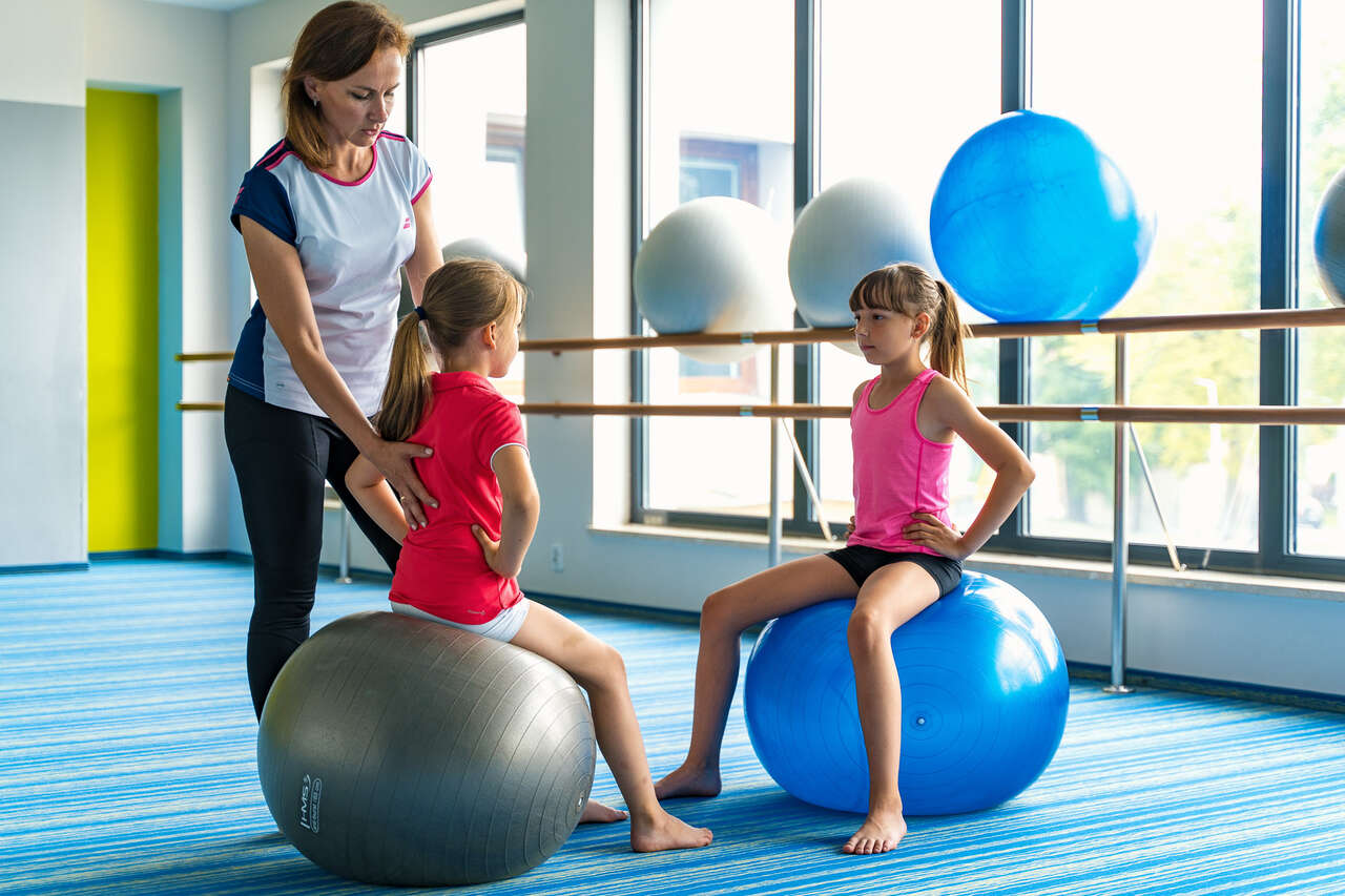 dr Ewa Waldzińska prowadząca zajęcia korekcyjne z dwiema młodymi dziewczynkami na sali fitness