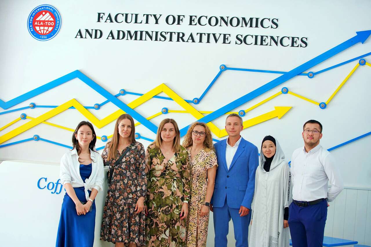 Grupa pracowników stojących przed logo uczelni Ala-Too International University w Kirgistanie