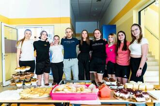 azdjęcie przedstawia grupę studentów i stół ze słodkościami